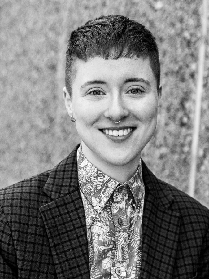 Headshot of Ryn, a white non-binary person with short hair, smiling and wearing a button-up collared shirt and a blazer